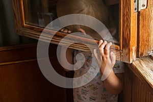 A small child is afraid of punishment and hides behind a window frame