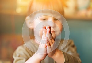 A small child asks. The baby girl clasped her hands together for prayer and supplication. Blurry Funny cute little girl praying at