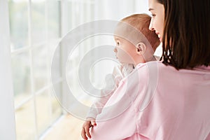 A small child, a boy, a baby in his mother's arms looks out the window