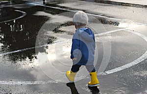 A small child boy going through puddles on a rainy day