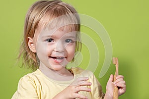 A small child brushes his teeth with an eco-friendly brush on a green background