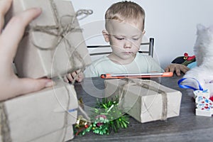 A small child with Christmas gifts is sitting at a New Year's wooden table with a tablet in his hands