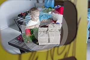 A small child with Christmas gifts is sitting at a New Year's wooden table with a tablet in his hands