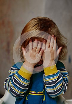 A small child cries, closing his eyes with his hands