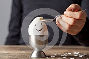 A small child is eating soft boiled humpty dumpty egg placed in egg cup on a wooden breakfast table
