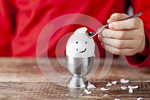 A small child is eating soft boiled humpty dumpty egg placed in egg cup on a wooden breakfast table