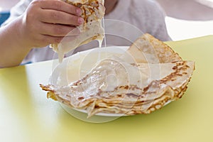 A small child eats a delicious pancake for breakfast with condensed milk. Appetizing pancakes for a children`s breakfast
