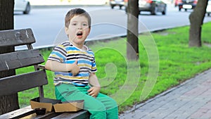 A small child eats French fries on a city street, sitting on a bench. Drops food to the ground. Fast food for kids