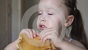 A small child eats a pancake in the kitchen while sitting at the table. Flour products. Tasty food. Close-up