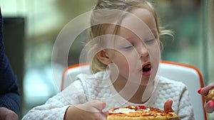 A small child in a fast food cafe eats pizza. Cute little kid girls portrait funny eating in fast food court in a mall