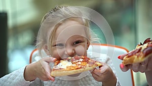 A small child in a fast food cafe eats pizza. Cute little kid girls portrait funny eating in fast food court in a mall