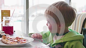 A small child in a fast food cafe eats pizza. pizza with cheese, ham, tomatoes and herbs in the dish on white background