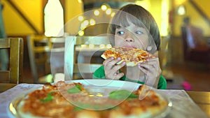 A small child in a fast food cafe eats pizza. Portrait of cute funny little caucasian kid boy eating delicious Italian
