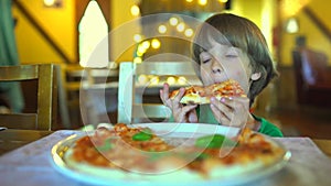 A small child in a fast food cafe eats pizza. Portrait of cute funny little caucasian kid boy eating delicious Italian