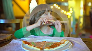 A small child in a fast food cafe eats pizza. Portrait of cute funny little caucasian kid boy eating delicious Italian