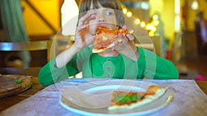 A small child in a fast food cafe eats pizza. Portrait of cute funny little caucasian kid boy eating delicious Italian