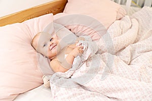 Small child girl calmly lies in bed with a toy under the covers and rests