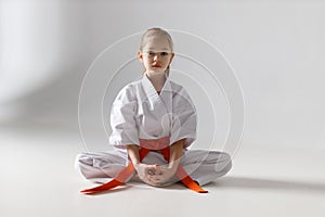 A small child girl karate student sits on a white background in a kimono