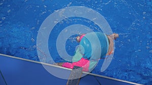 Small child girl is learning to swim in pool diving and floating in water.