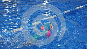Small child girl is learning to swim in pool diving and floating in water.