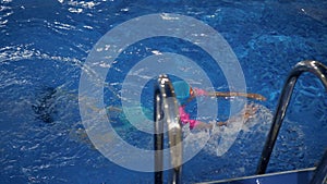 Small child girl is learning to swim in pool diving and floating in water.