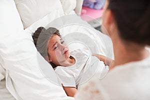 Small child is girl, lying in bed and crying violently. Mother comforts child
