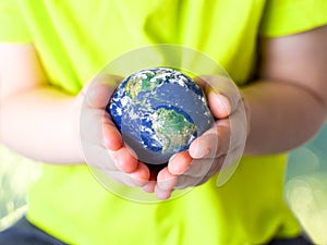 Small child in a green T-shirt holding the planet Earth in her hands. Earth day. Green concept