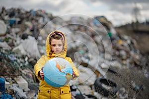 Small child holding globe on landfill, environmental pollution concept.