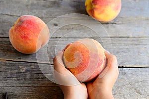 Small child holds a ripe peach in his hand. Juicy bright peaches on an old wooden table. Delicious and vitamin dessert for child