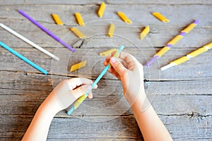 Small child holds straw and dried tube pasta in his hands. Child stringing pasta onto straw