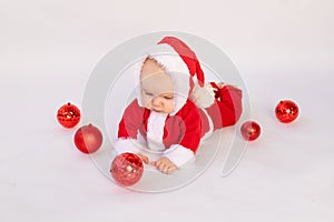 A small child lies in a Santa costume on a white isolated background with red Christmas balls, space for text, Christmas concept