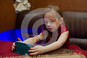 Small child looking at cell phone. Little girl in a burgundy dress looks at the phone