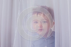 the small child looks through a curtain in the room