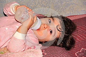 Small child lying and drinking milk product from bottle