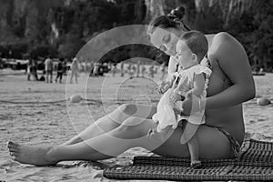 A small child is naughty and cries while sitting on the hands of mom. On the beach. Black and white photography