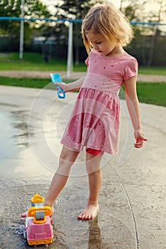 Small child at playground in public park playing with toys and water. Little girl at splash pad in summer