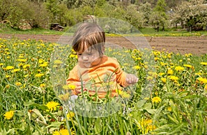 Small child playing on a green meadow surrounded with yellow flowers