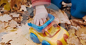 Small child is playing with a toy car in an autumn park. Cool weather