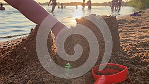 A small child plays on the beach near a pond at sunset.