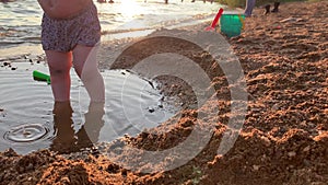 A small child plays on the beach near a pond at sunset.