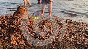 A small child plays on the beach near a pond at sunset.