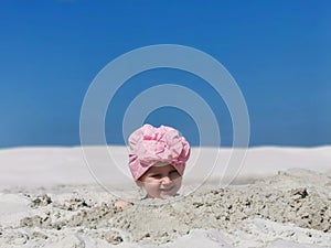 a small child plays in the sand on the beach, buried up to his head, a girl in a scarf smiles while playing