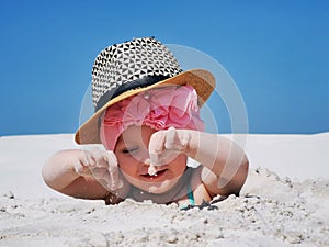 a small child plays in the sand on the beach, buried up to his head, a girl in a scarf smiles while playing