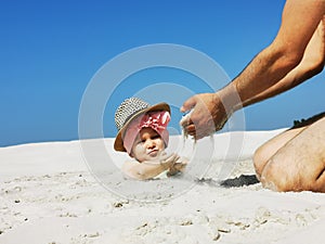 a small child plays in the sand on the beach, buried up to his head, a girl in a scarf smiles while playing