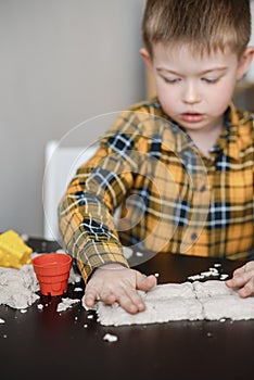 A small child plays in the sandbox at home. Boy makes sand molds