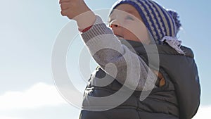 A small child plays with toys on the sea shore in winter clothes and a hat.