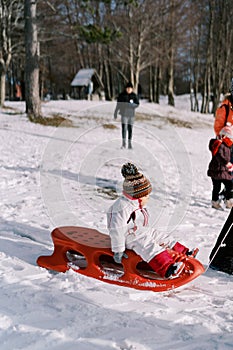 Small child rides on a sled holding on to the sides and looks ahead