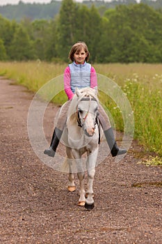 Small child riding on a white horse on the road Outdoors