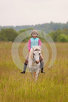 Small child riding on a white horse and smiling Outdoors