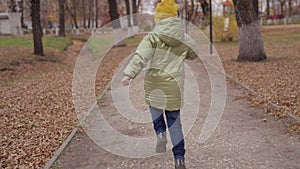 A small child runs along the road in a city park in autumn, a happy family, a cheerful childhood, a joyful kid jumps up